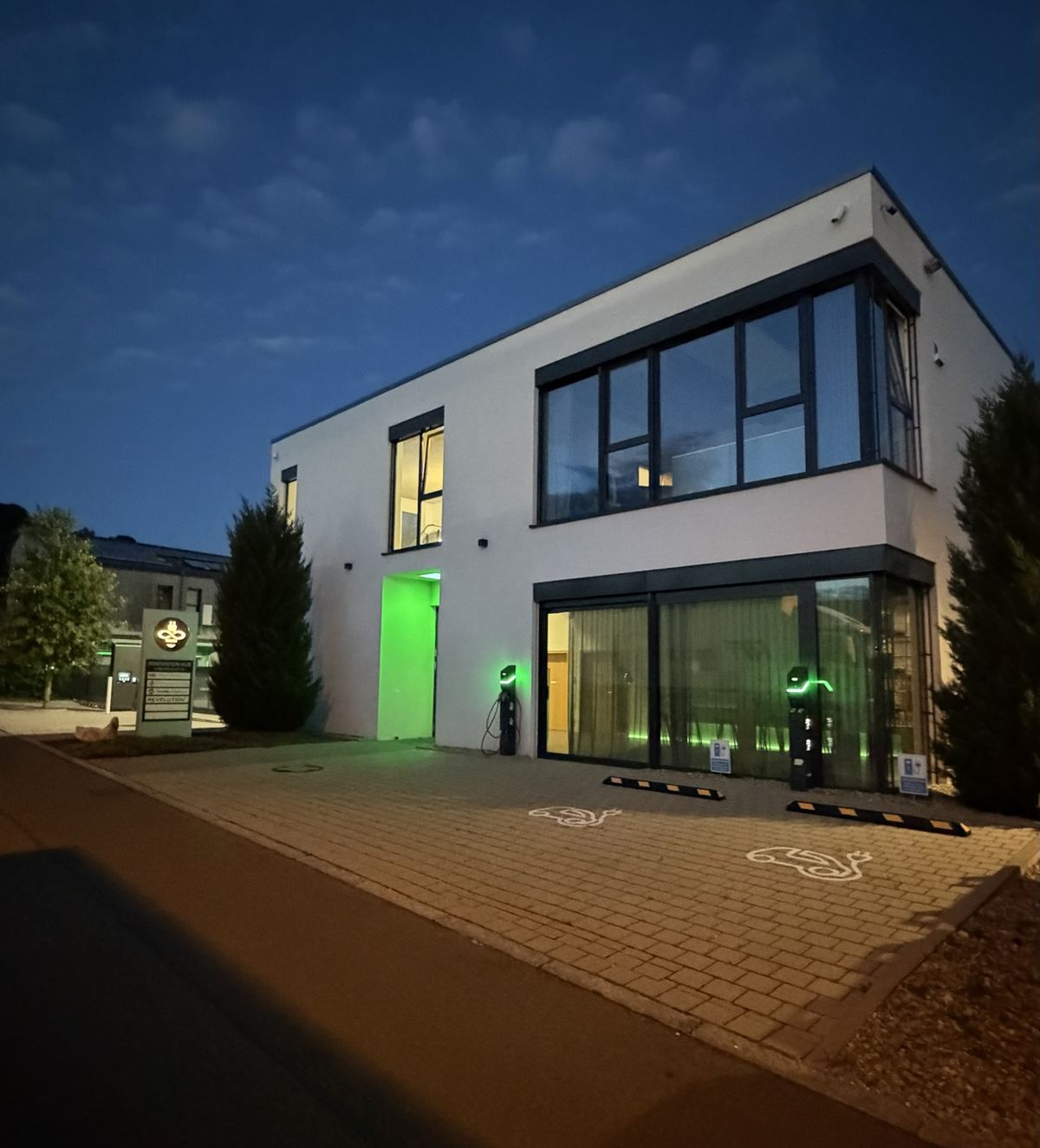 Innovation HUB bei Nacht mit beleuchtetem Eingang und Ladepunkten